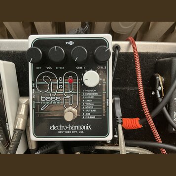 Bílý efekt pedál s černým předním panelem a nápisem bass machine 9:9. Na spodní části je logo electro-harmonix NEW YORK CITY, USA. V horní části jsou…