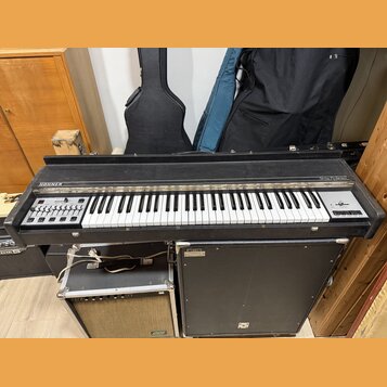 Černý klávesový nástroj s bílými a černými klávesami. Na levé straně je nápis HOHNER a na pravé straně nápis String Performer. V levé části se nacház…