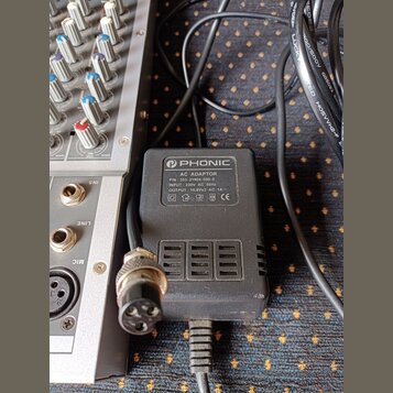 Černý síťový adaptér značky PHONIC s bílým štítkem. Na štítku je text: AC ADAPTOR, P/N: 353-21904-000-0, INPUT: 230V AC 50Hz, OUTPUT: 16.8Vx2 AC 1A a…