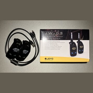 Na fotografii je bezdrátový systém pro kytaru značky JOYO, model JW-03, v originálním balení. Sada obsahuje černý vysílač s nápisem JOYO TRANSMITTER…