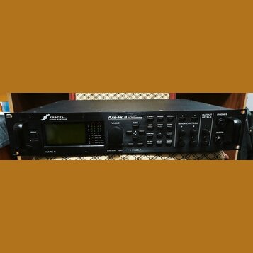 Černý rackový procesor s nápisy FRACTAL AUDIO SYSTEMS a Axe-Fx II PREAMP/ FX PROCESSOR. Na předním panelu je displej, ovládací knoflíky a tlačítka s…