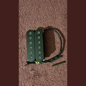 Černý humbucker s dvěma řadami šesti polových magnetů. Na spodní části levého snímače je svisle napsaný nápis DiMarzio. K nástroji vedou černé vodiče…