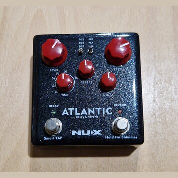 Kytarový efekt pedál s černým třpytivým povrchem a červenými ovládacími knoflíky. Na spodní části je bílý nápis ATLANTIC delay & reverb a logo NUX. V…