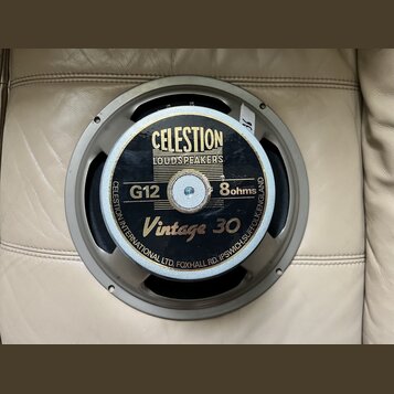 Kruhový reproduktor s šedým kovovým rámem. Na černém středovém štítku je zlatý nápis CELESTION LOUDSPEAKERS, označení G12, 8ohms a model Vintage 30.…
