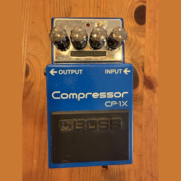 Modrý efekt pedál s nápisy Compressor a CP-1X. Na spodní části je černý gumový spínač s vyraženým logem BOSS. Horní ovládací panel obsahuje čtyři chr…
