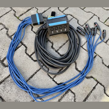 Sada kabelů s rozbočovacím černým boxem, který má čtyři konektory XLR. Na boxu jsou vidět bílé nápisy 1, 2, 3 a 4. Z boxu vychází černý kabel, který…