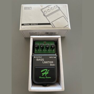 Efektový pedál v bílém kartonovém boxu s nápisem PEDAL EFFECT a nákresem komba. Pedál je zelený a černý s nápisy OUTPUT, INPUT, BASS LIMITER a BLM-I.…