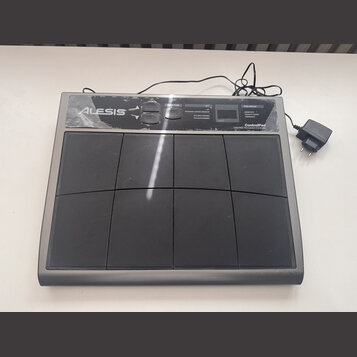 Šedý MIDI kontrolér s osmi černými gumovými pady. V levém horním rohu je bílé logo ALESIS a v pravém horním rohu nápisy ControlPad, USB/MIDI Percussi…