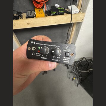 Černý osobní sluchátkový zesilovač s nápisem P1 PERSONAL IN-EAR MONITOR AMPLIFIER a logem behringer. Zařízení má dva ovládací knofíky s popisky VOLUM…