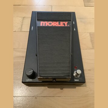 Černý wah pedál značky MORLEY s žebrovaným povrchem šlapací plochy. Na horní části je červené logo MORLEY a nápisy OUT, IN a 9V. V dolní části se nac…