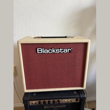 Kytarový kombozesilovač s krémovým vinylovým potahem a červenou texturovanou přední síťovkou. Uprostřed sítě je umístěno bílé logo Blackstar. Zesilov…