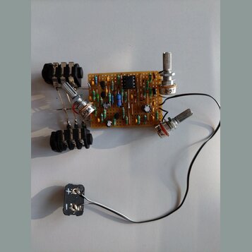 Fotografie zobrazuje ručně sestavený elektronický obvod na hnědé perforované desce s různými součástkami. Na desce jsou připájena tři potenciometry,…