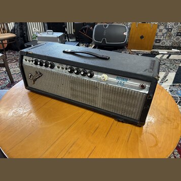 Kytarový kombozesilovač s černým texturovaným potahem a stříbrným předním panelem. Na levé straně je viditelné logo Fender a vpravo nápis BASSMAN 135…