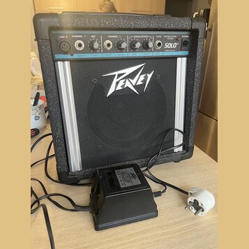 Černý přenosný kombozesilovač s logem Peavey na předním mřížkovém krytu. Horní ovládací panel obsahuje nápisy LOW Z, CHANNEL 1, MIC, CHANNEL 2, EQUAL…