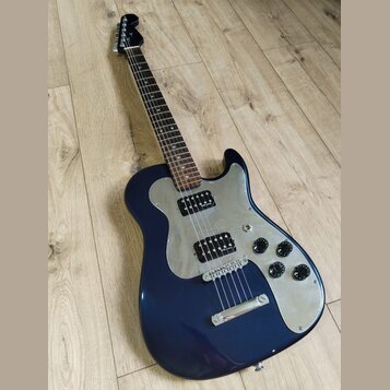 Tmavě modrá elektrická kytara s kovovým pickguardem a hnědým hmatníkem. Nástroj má dva humbuckery, tři ovládací knofíky a jeden přepínač. Na hlavě kr…