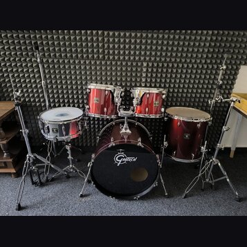 Vícedílná bicí souprava v tmavě červené barvě s chromovaným kováním. Na basovém bubnu je bílé logo Gretsch, stejné logo je viditelné i na ostatních b…
