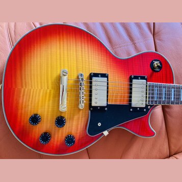 Elektrická kytara s trupem v červeno-žlutém sunburst provedení a viditnou strukturou dřeva. Nástroj má dva humbuckery s kovovými kryty, černý pickgua…
