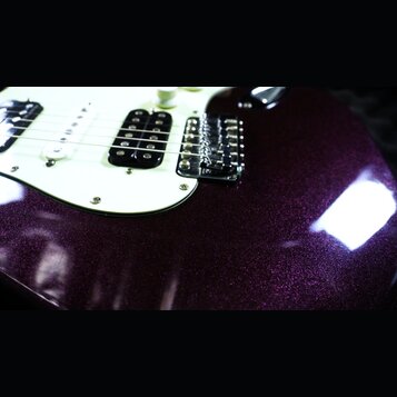 Detail elektrické kytary s tmavě fialovým metalizovaným povrchem s třpytivým efektem. Nástroj má bílý pickguard, tři snímače (dva jednoduché a jeden…