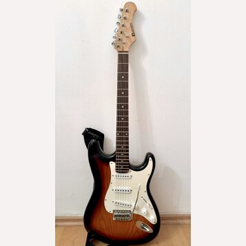Elektrická kytara s tłem v provedení sunburst a bílým pickguardem. Na hlavě hředu je viditelné logo "Squier". Nástroj má tři snímače typu single-coil…