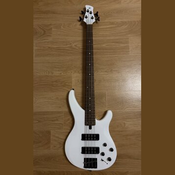 Bílá elektrická basová kytara s tmavým hnedým hmatníkem. Na hlavě je viditelné logo Yamaha. Nástroj má dva černé humbuckery, tři černé ovládací knofl…