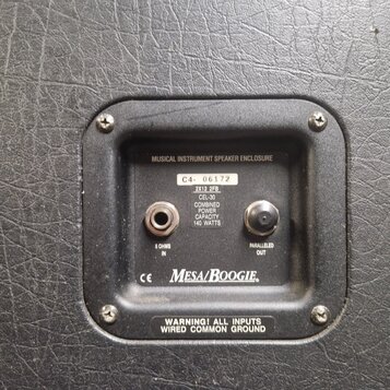 Detail zadní strany kytarové reprobedny potažené černým vinyllem. Na černé plastové panelu jsou dva jack konektory s nápisy 8 OHMS IN a PARALLELED OU…