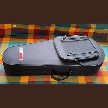 Černý pol pevný pouzdro na hudební nástroj s rukojetí. Na povrchu je bílý obdélníkový štítek s červeným nápisem GIGBAG CASES. V horní části je připev…