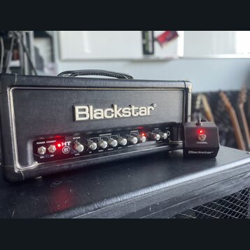 Černý kytarový zesilovač s nápisem Blackstar na předním panelu. Pod logem se nachází ovládací prvky s nápisy POWER, STANDBY, HT 5, REVERB (LEVEL), EQ…