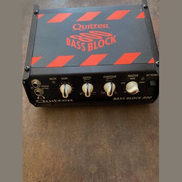 Černý basový zesilovač s červenými šikmými pruhy na horní straně. Na vrchu je nápis Quilter BASS BLOCK 800 a na předním panelu vpravo text BASS BLOCK…