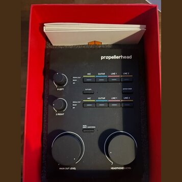 Černý zvukový interface značky propellerhead v červené krabici. Zařízení má dva menší ovratidla s popisky 1/LEFT a 2/RIGHT, dvě velká ovratidla MAIN…