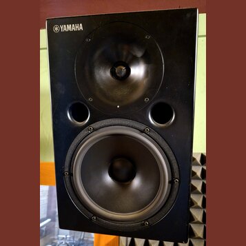 Černý reproduktor s logem YAMAHA v levém horním rohu. Je vybaven jedním výškoveým a jedním basovým reproduktorem, mezi kterými jsou umístěny dva kula…