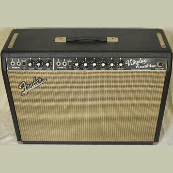 Kytarový zesilovač v černém krytu s béžovou textilní mřížkou. Na ovládacím panelu jsou nápisy Vibrolux Reverb Amp, FENDER MUSICAL INSTRUMENTS a DESIG…