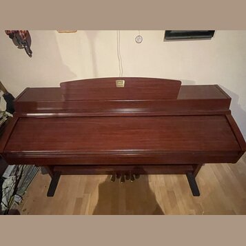 Hnědé dřevěné piano s uzavřenou klaviaturní víkem. V horní části je umístěno zlaté logo s nečitelným nápisem. Nástroj stojí na dvou černých nohách a…