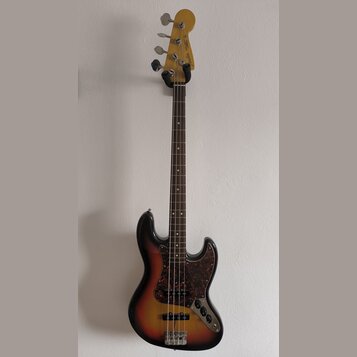 Elektrická basová kytara s tělem v provedení sunburst a hnědým hracím hřidlem. Tělo má tmavý vzorovaný pickguard a na hlavě je viditelné logo Fender.…