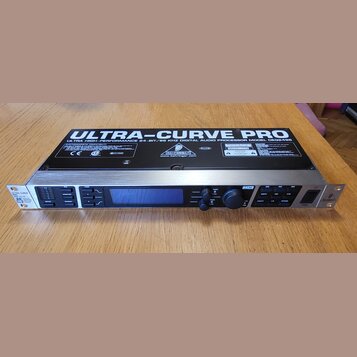 Digitální audio procesor v rackovém provedení s černým šasi a stříbrným předním panelem. Na horní straně je nápis ULTRA-CURVE PRO a text ULTRA HIGH-P…