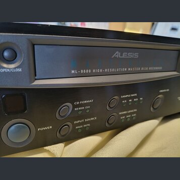 Černý digitální nahrávací zařízení s nápisem Alesis MASTERDISK ML-9600 HIGH-RESOLUTION MASTER DISK RECORDER. Na předním panelu jsou tlačítka POWER, O…