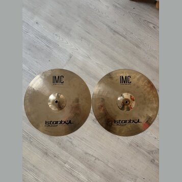 Dvě mosazné činely typu hi-hat položené vedle sebe na světlé podlaze. Oba mají identické nápisy: v horní části „IMC 13" BRILLIANT HI-HAT“ a v dolní č…