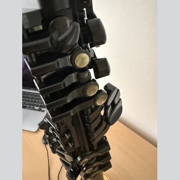 Detailní záběr na mechanismus černého dechového nástroje, pravděpodobně klarnetu. Jsou vidět kovové klapy s perleťovými vložkami a černé plastové neb…