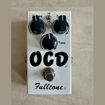 Bílý kytarový efekt s nápisem OCD a logem Fulltone. Na horní straně jsou tři černé otočné ovnovky s popisky Volume, Drive a Tone. Mezi nimi jsou umís…