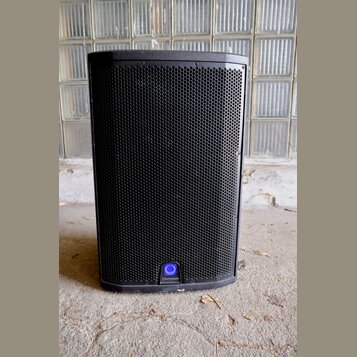 Černý reproduktor v hranatém provedení s kovovou mřížkou. Ve spodní části je umístěno kulaté modré logo s nápisem Q Turbosound. Povrch je v dobrém st…