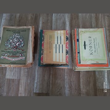 Tři staré notové seпиты položené na dřevěné podlaze. První kniha zleva má nápis „Česká opera pro mladé pianisty“, „B. SMETANA“ a „PRODANÁ NEVĚSTA“. P…
