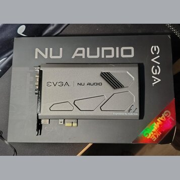 Šedá zvuková karta s kovovým krytem, položená na černém kartónovém obalu. Na krytu i na obalu je uveden nápis EVGA NU AUDIO a v pravém dolním rohu kr…