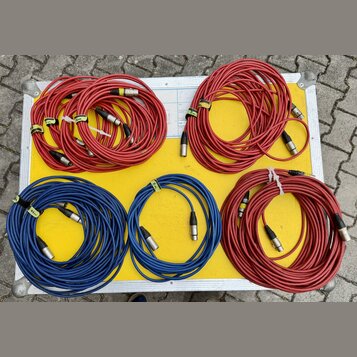 Pět svátků audio kabelů s XLR konektory, položených v otevřeném transportním kufru. Kabely jsou v červené a modré barvě, část z nich má bílé papírové…