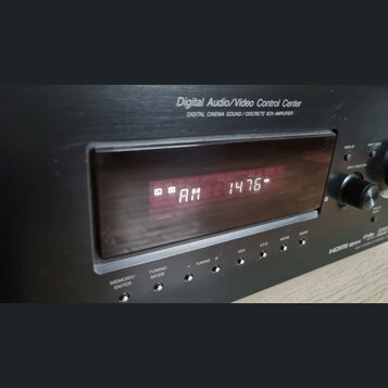 Černý Digital Audio/Video Control Center s nápisem DIGITAL CINEMA SOUND / DISCRETE 5CH AMPLIFIER. V displeji svítí červeným text AM 1476. Pod displej…