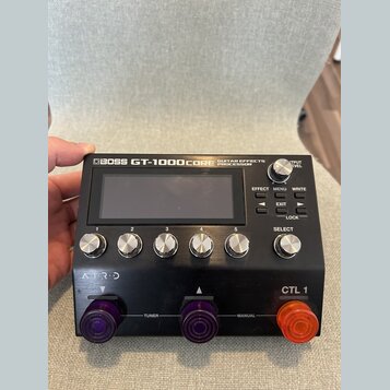 Černý kytarový procesor s nápisem BOSS GT-1000CORE GUITAR EFFECTS PROCESSOR. Zařízení má centrální displej, pět očíslovaných otočných ovladačů (1–5),…