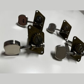 Čtyři kovové ladicí mechanismy s chromovanými knoflíky. Mechanizmy mají mosazný nebo pozlacený povrch s viditelným opotřebením a oxidací. Na dílech n…