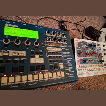 Modrý sekvenční modul s nápisy YAMAHA a RM1x SEQUENCE RECORDER MIXER. Zařízení má zelený podsvícený displej, několik otočných knoflíků a bílé orazvác…