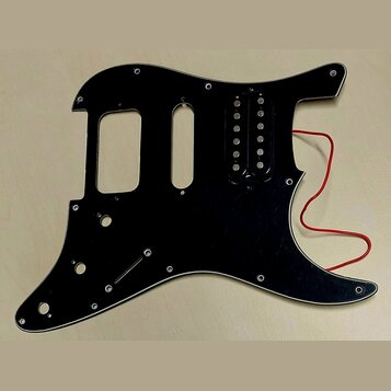 Černý plastový pickguard pro elektrickou kytaru s jedním instalovaným humbuckerem. Z povrchu jsou viditelné drobné škrábance a stopy používání, z nás…