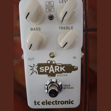 Bílý kytarový efekt s nápisem SPARK BOOSTER a logem tc electronic. Na horní straně jsou čtyři bílé otočné knoflíky s popisky LEVEL, BASS a TREBLE, dá…