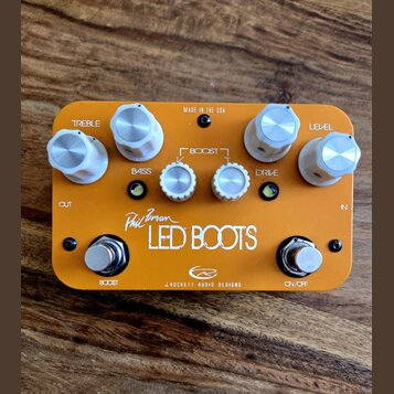 Kytarový efekt pedál v oranžovém provedení s bílými plastovými knoflíky. Na povrchu jsou nápisy TREBLE, BASS, BOOST, DRIVE a LEVEL, v dolní části je…