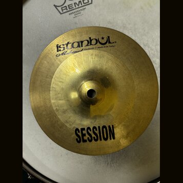 Zlatavý kovový činel s nápisem istanbul® a pod ním menším písmem Mahmet Handmade Cymbals from Turkey. Ve spodní části je uveden model SESSION. Činel…